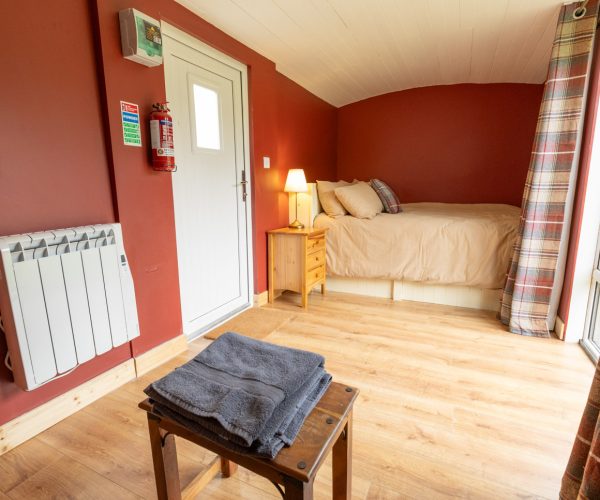 Cozy bedroom with a single bed, wooden floor, red walls, and folded towels on a stool.