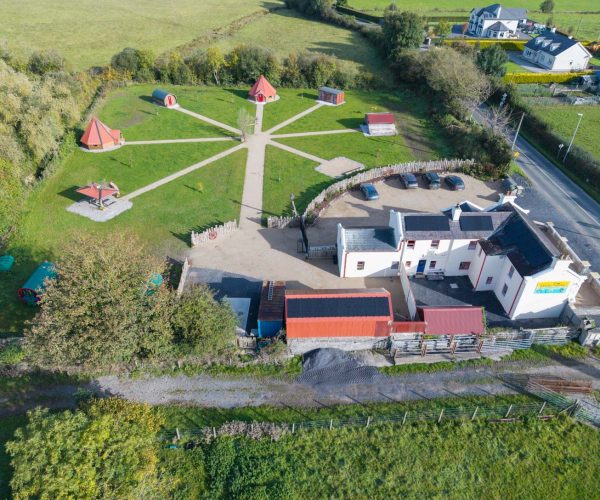 Aerial view of a small rural complex with red cabins arranged in a circle on green grass.